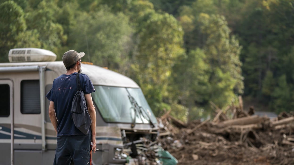 A man stares out at a piece of land full of debris, including the rubble of a home and a destroyed RV.