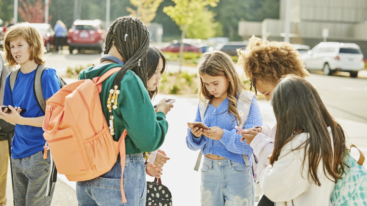 Teens gathered outside of school, all staring at their phones together.