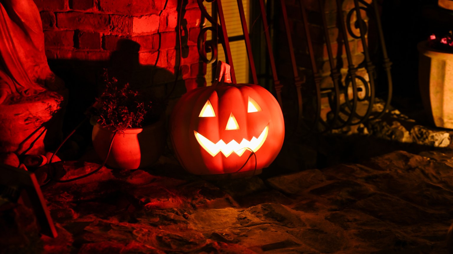 A glowing carved pumpkin sits against a brick wall in the dim light.