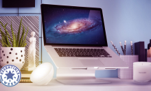 Laptop on a computer stand surrounded by a bowl-shaped light, a scented candle, and a plant