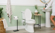 Green bathroom with toilet and bidet attachment and person standing in corner