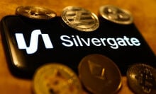 Silvergate logo displayed on a phone screen, surrounded by coins representing cryptocurrencies.