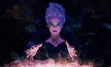 A sea witch wearing a bedazzled black dress stands in front of a glowing cauldron. 