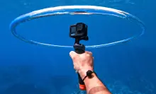 a right hand holds a gopro in a ring of air underwater