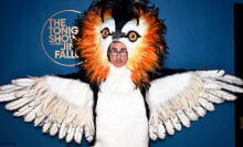 A man in glasses is dressed up as a large bird with an impressive orange plumage.