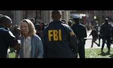 A man in an FBI jacket walks through a crowd.