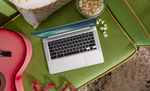 a top-down view of an hp chromebook sitting on an olive green couch next to a pink guitar and a spilled bowl of popcorn