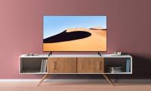 Samsung 4K TV with sand dune screensaver sitting on TV stand with pink wall in background