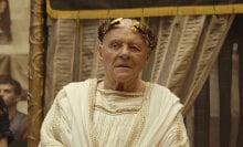 A man dressed in a white robe with a gold crown, like a Roman emperor.