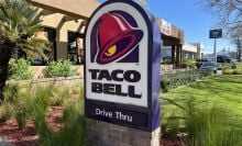 Taco Bell drive-thru open for business with lush green plants and clear sky in a residential neighborhood