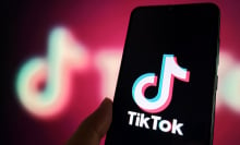 A phone displaying the TikTok logo in front of a blurry pink-hued TikTok logo.