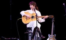 Clairo smiling as she plays the guitar on stage.