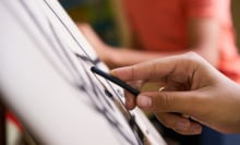 A close-up of a person's hand holding charcoal as they draw on an easel at an art class. 