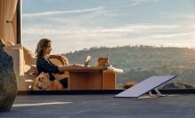 a starlink wifi satellite sits on a wooden deck while a woman works on a laptop in the background with her dog