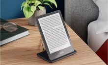 the kindle paperwhite signature edition sits on a wireless charger on a nightstand.