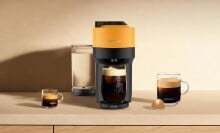 a mango-colored nespresso machine sits on a kitchen counter with several cups of coffee around it