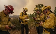 Four firefighters stand in a circle looking down at radios and notepads. 