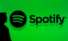 The silhouette of a man in front of a bright green backdrop that reads, "Spotify" with the Spotify logo next to it. 