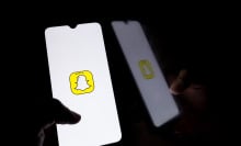 A hand holds a glowing phone showing the Snapchat logo in a dark room.