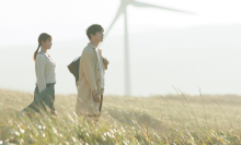 A still from 'Beyond Goodbye' of a man and woman in a field, with wind turbines in the background.