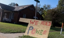 A wooden sign that reads "We need power" on the lawn outside of a home.