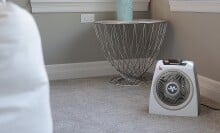 a vornado space heater sits on a carpeted floor in a brightly lit bedroom with natural light