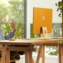 Mac sitting at desk working on yellow Apple iMac 24-inch computer