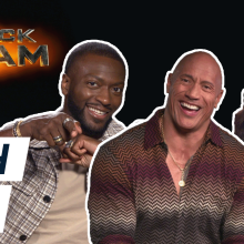 Dwayne Johnson, Sarah Shahi and Aldis Hodge smiling in front of the Black Adam title