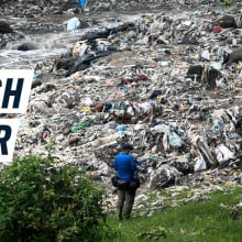 A man stands in front of a river which resembles a mountain of plastic more than a body of water. Caption reads: "Trash River"