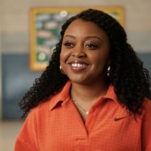 Janine Teagues from "Abbott Elementary" standing in a hallway in an orange blouse.