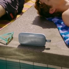 Person laying next to Bose Bluetooth speaker by the pool.