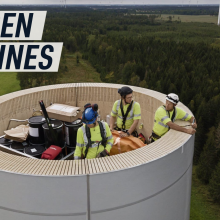 An aerial shot shows workers standing inside a wooden wind turbine as it is being constructed.