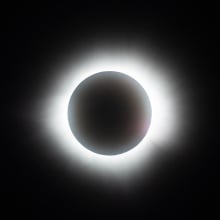 The sun fully disappears behind the moon during the solar eclipse. The light behind the moon is white and bright.