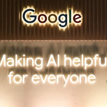 People in front of the Google logo on a wall above a slogan about making AI helpful for everyone