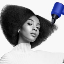 person using blue dyson supersonic hair dryer to style their hair