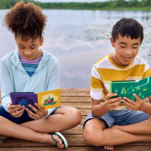 Two kids sit by the water reading their Kindles