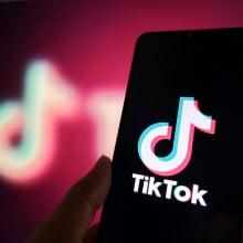 A phone displaying the TikTok logo in front of a blurry pink-hued TikTok logo.