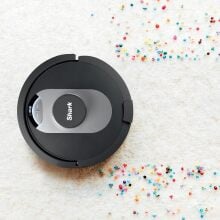 a shark robot vacuum cleans a white carpet