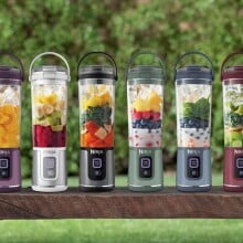 a lineup of ninja portable blenders that are various colored and filled with various smoothie ingredients, sitting in each blender unblended