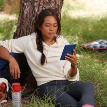 A girl sits outside and reads on her Amazon Kindle 