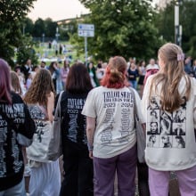 Taylor Swift fans decked out in merch standing in a crowd. 