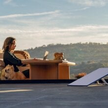 a starlink wifi satellite sits on a wooden deck while a woman works on a laptop in the background with her dog