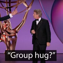 Two men and a woman stand on an awards show stage.