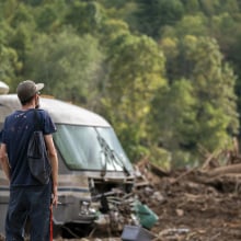 A man stares out at a piece of land full of debris, including the rubble of a home and a destroyed RV.