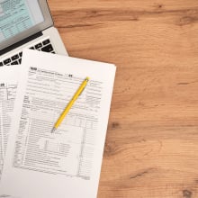 Tax paperwork on a table next to a laptop.