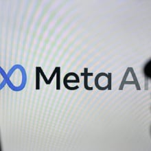 A person holding a cell phone in front of the Meta AI logo displayed on a computer screen, on April 29, 2024, in Edmonton, Canada.