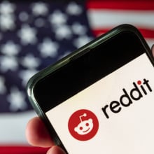 A phone displaying the Reddit logo in front of an American flag.