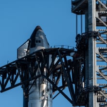 A large metal structure holds up the Space X Starship against a blue sky.