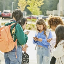 Teens gathered outside of school, all staring at their phones together.