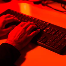 A hand typing on a keyboard bathed in red light. 